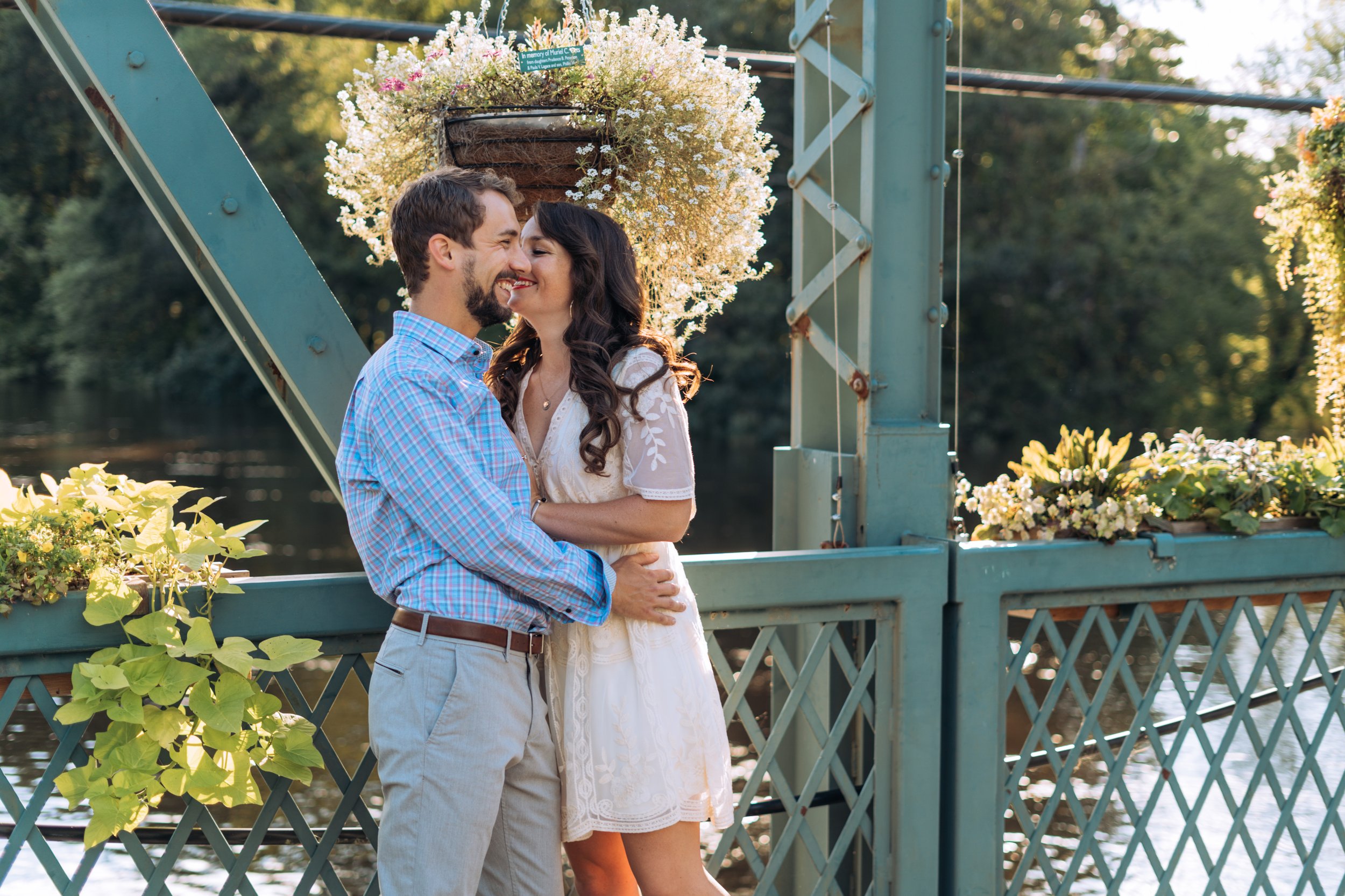 A straight white couple hugs on the Drake Hill Flower Bridge in Simsbury. The bridge is blue. The man is wearing a blue shirt and the woman is wearing a short white dress.