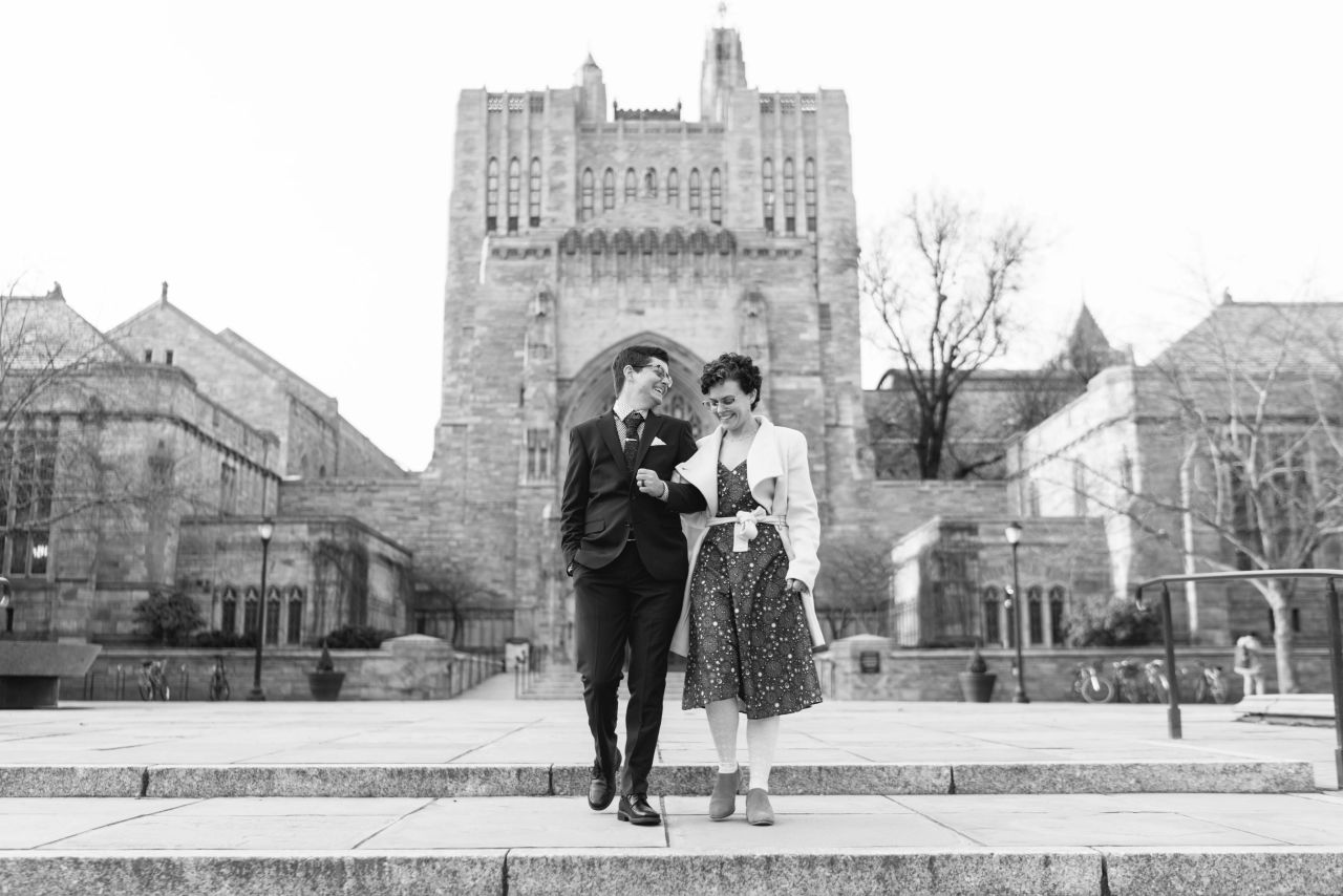 A white cis woman walks with a white trans man after eloping. They are walking down the stairs in front of the Yale Library.
