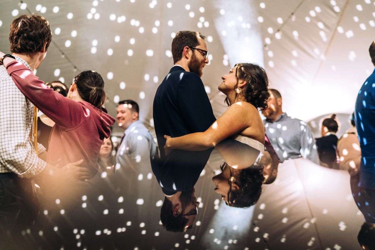 A newlywed bride and groom dance at their wedding with twinkly lights surrounding them.